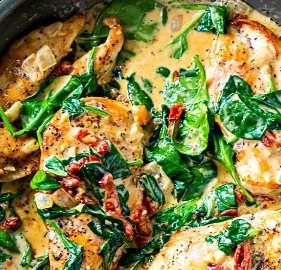 Creamy Tuscan chicken dish with herbs and vegetables in a bowl.