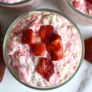 Strawberries and cream overnight oats in a glass, topped with fresh strawberries