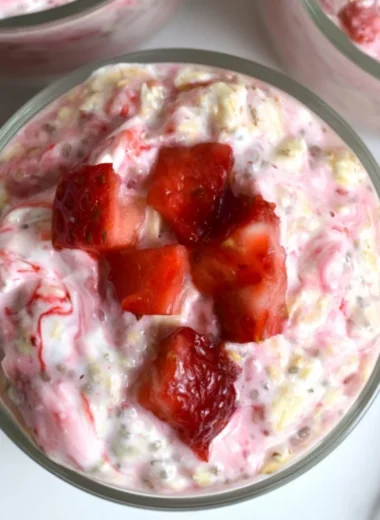 Strawberries and cream overnight oats in a glass, topped with fresh strawberries