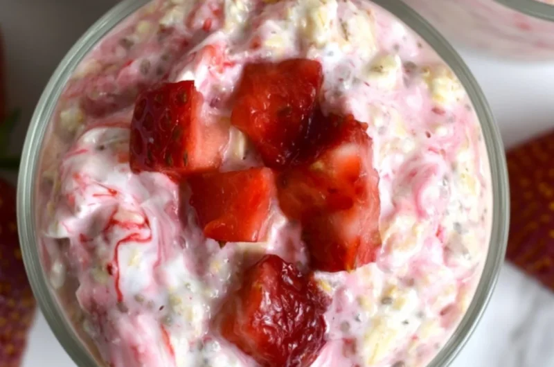 Strawberries and cream overnight oats in a glass, topped with fresh strawberries